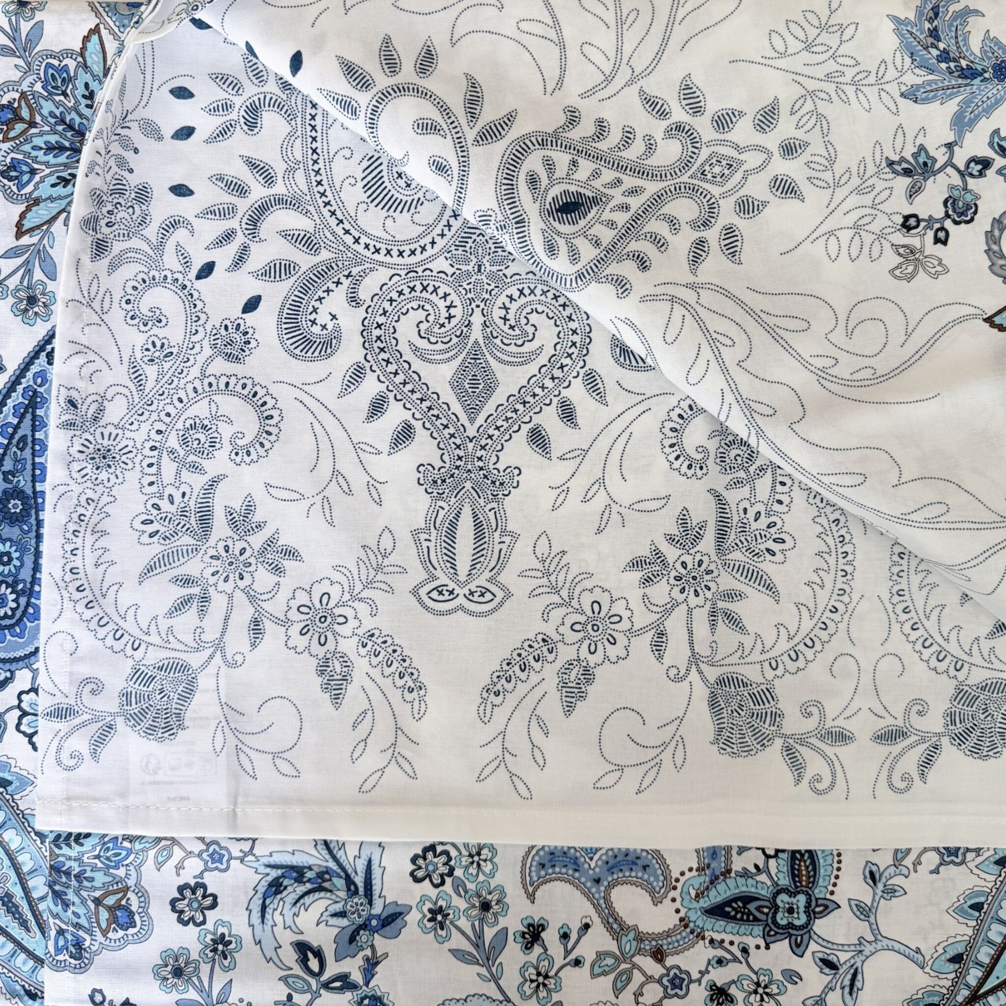 Dettaglio della fantasia Monnalisa Bassetti Granfoulard con elegante motivo paisley floreale su fondo bianco azzurro.