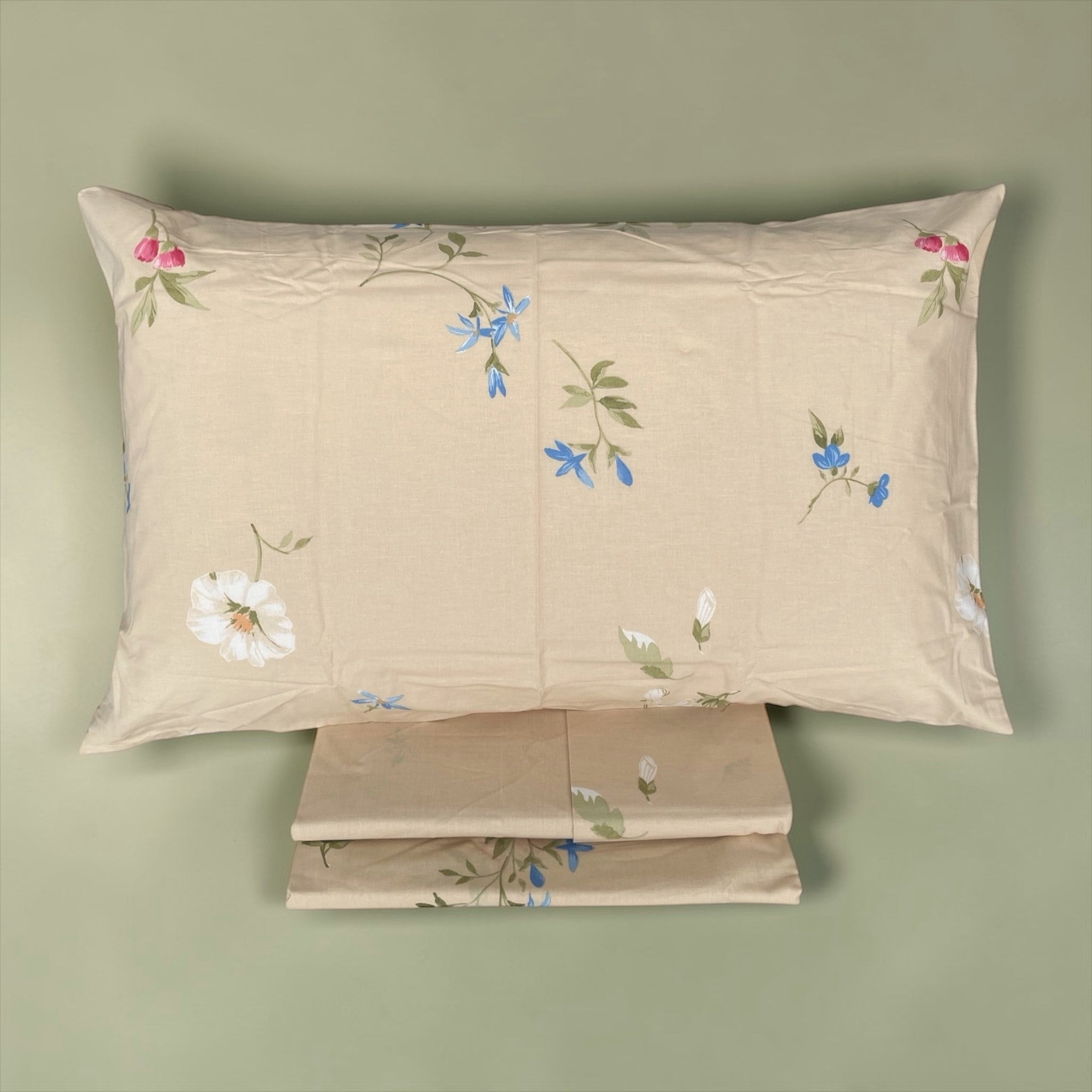 Federa Caleffi Floral 2 su fondo avorio con rametti verdi e fiori multicolore, accanto alle lenzuola ripiegate.