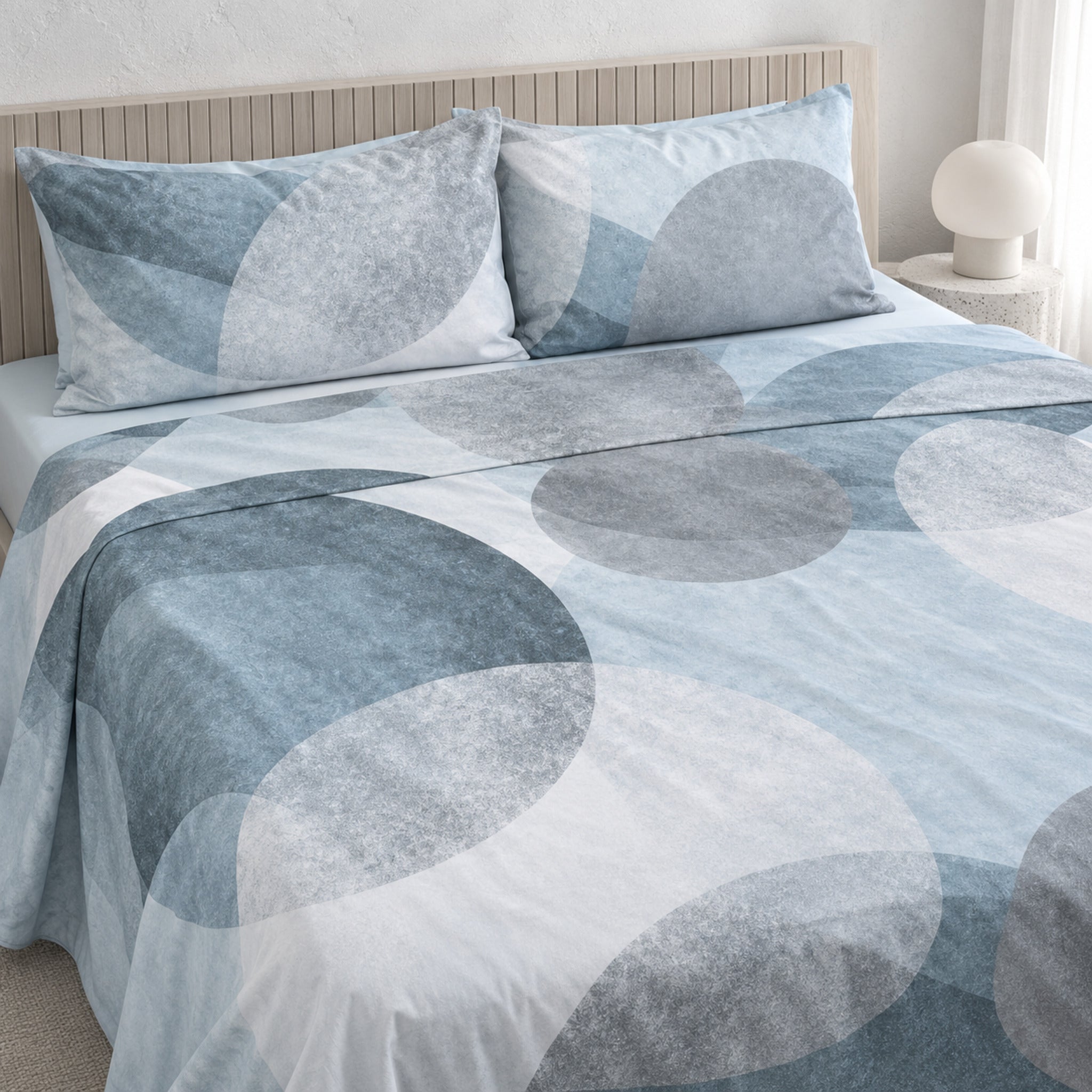 Lenzuola matrimoniali Cogal 2669 sul letto, con grandi cerchi sovrapposti blu, azzurri e grigi e federe coordinate