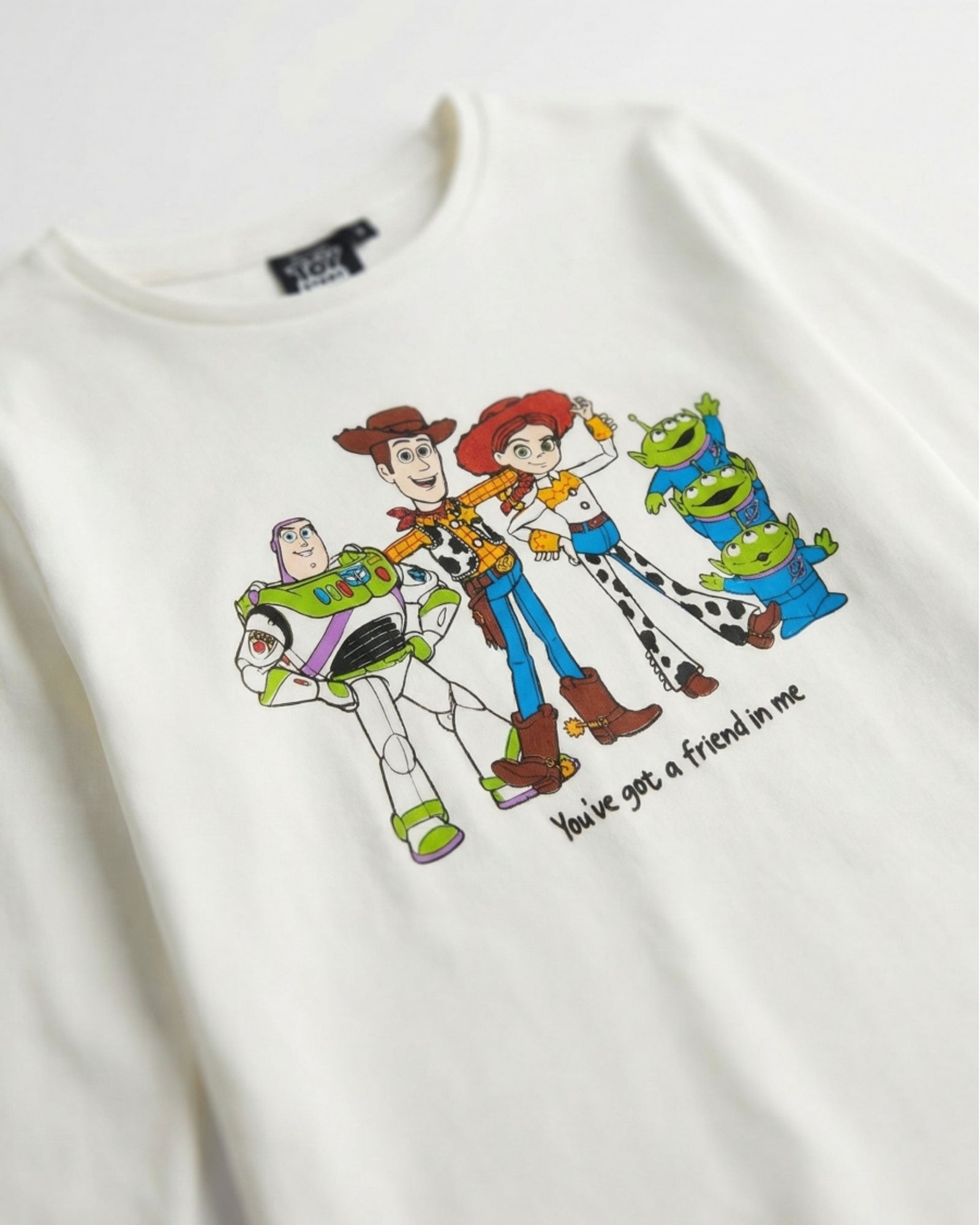 Dettaglio della maglia Toy Story 64892 con Woody, Buzz Lightyear, Jessie, alieni verdi e scritta You've got a friend in me.