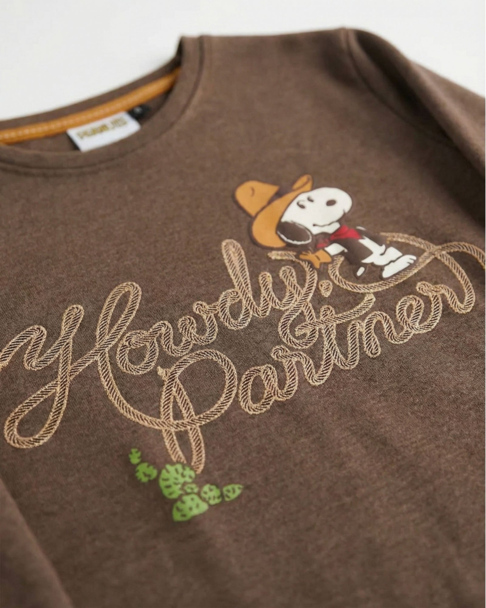 Dettaglio della maglia cioccolato mélange con Snoopy cowboy, cactus e scritta Howdy Partner con dettagli metallizzati.
