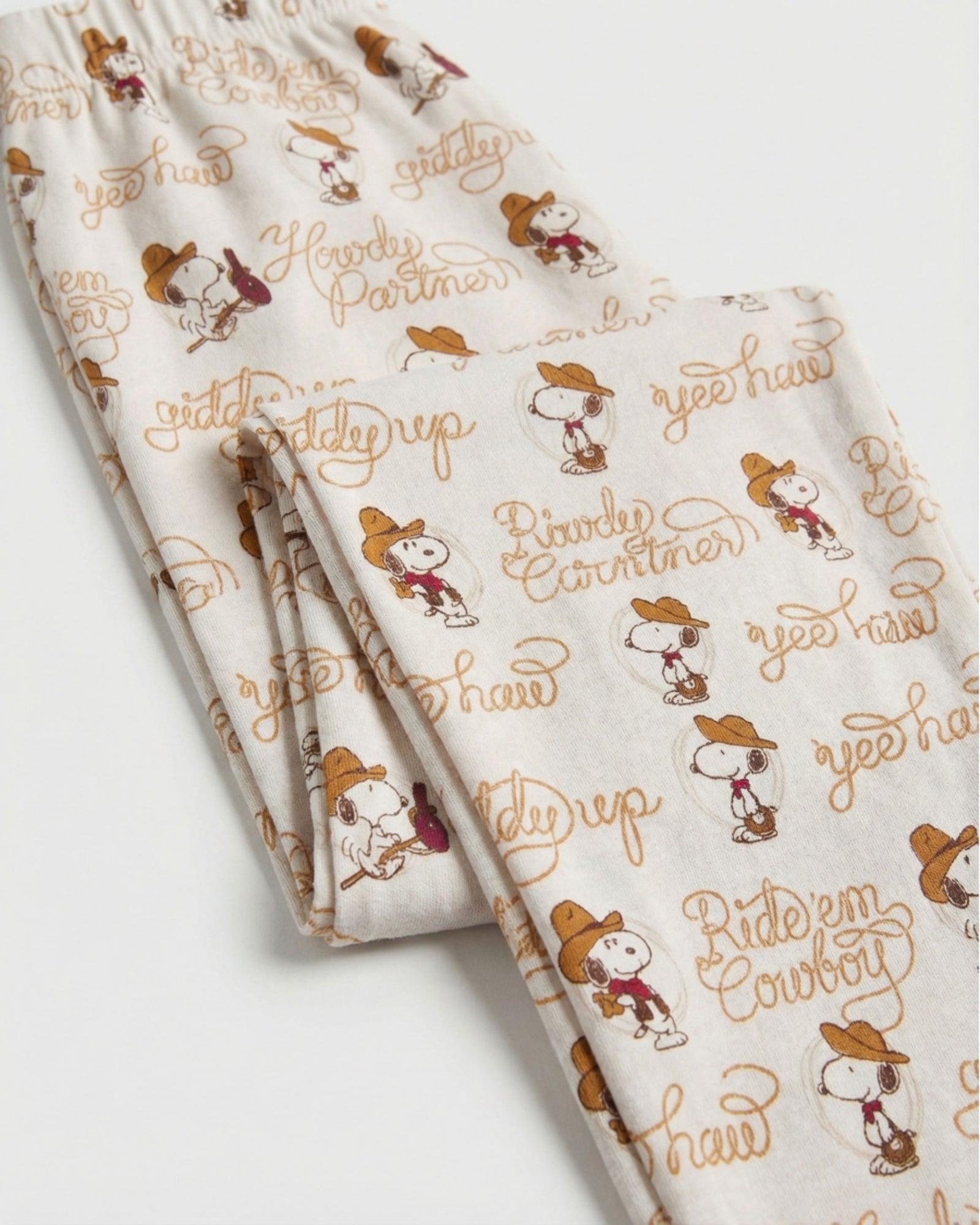 Dettaglio dei pantaloni del pigiama Peanuts 64036, con elastico in vita e fantasia Snoopy cowboy su fondo chiaro.