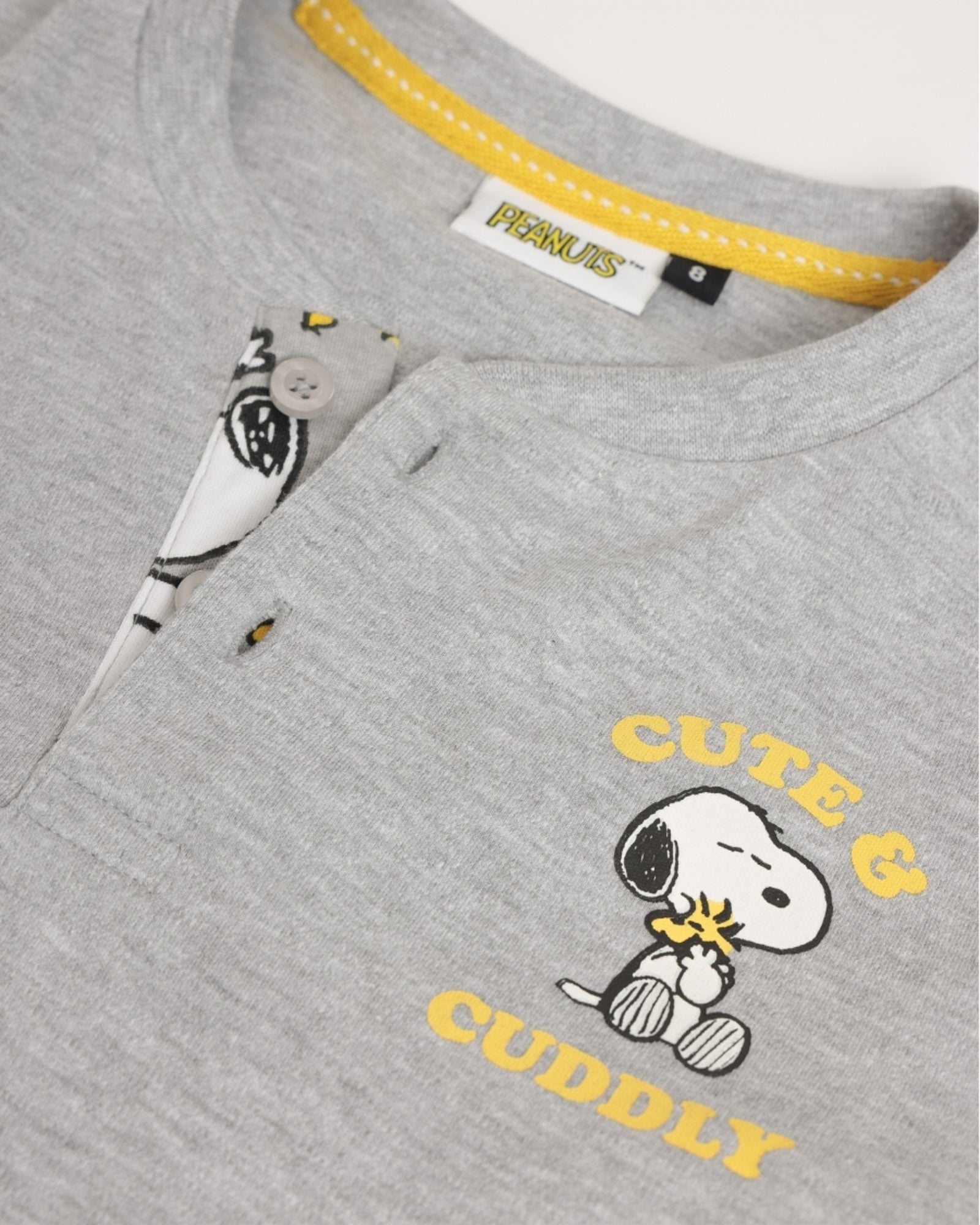 Dettaglio della maglia grigio mélange con apertura a bottoni, stampa Snoopy e Woodstock e scritta gialla Cute & Cuddly