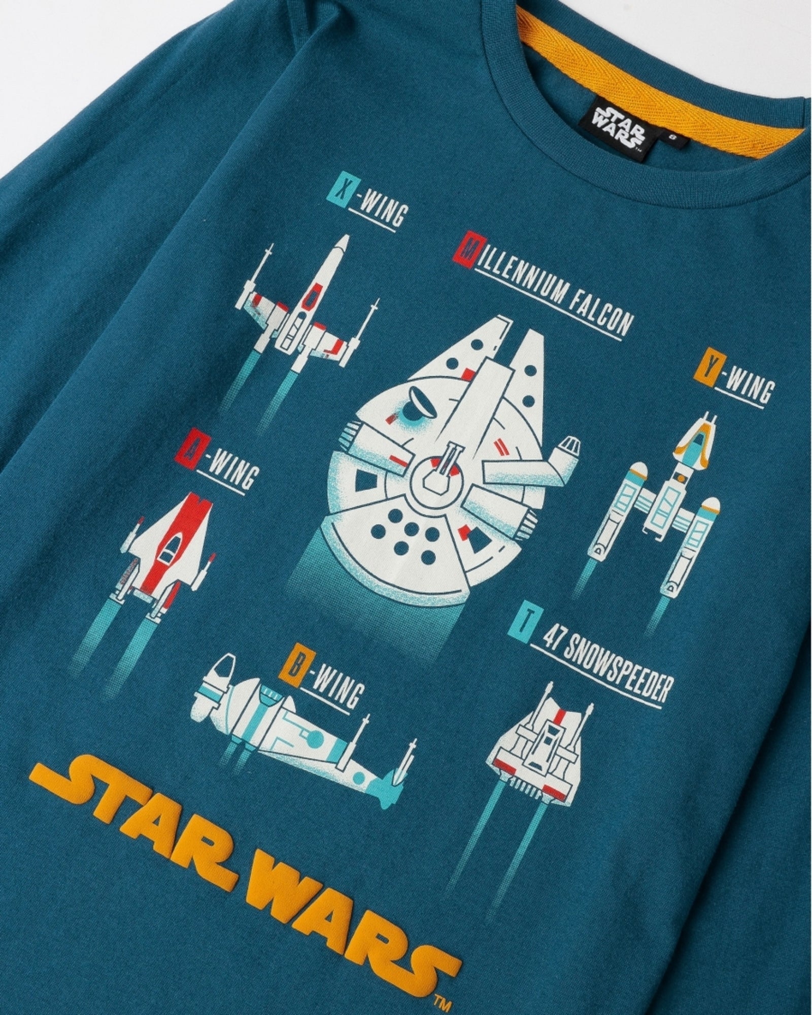 Dettaglio della maglia blu oceano con Millennium Falcon, X-wing e altre astronavi, girocollo e logo Star Wars giallo
