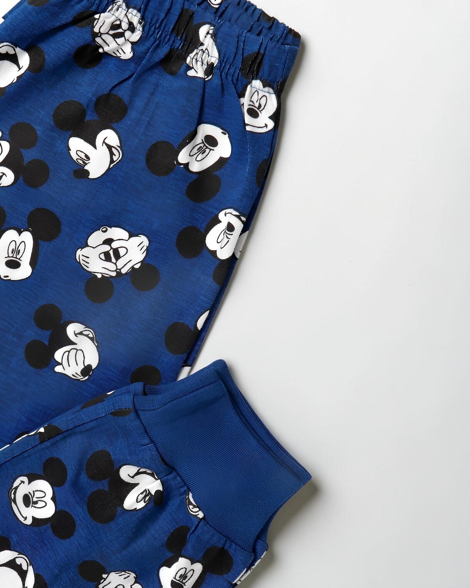 Dettaglio dei pantaloni blu con vita elasticizzata, stampa dei volti di Mickey Mouse e polsino al fondo gamba