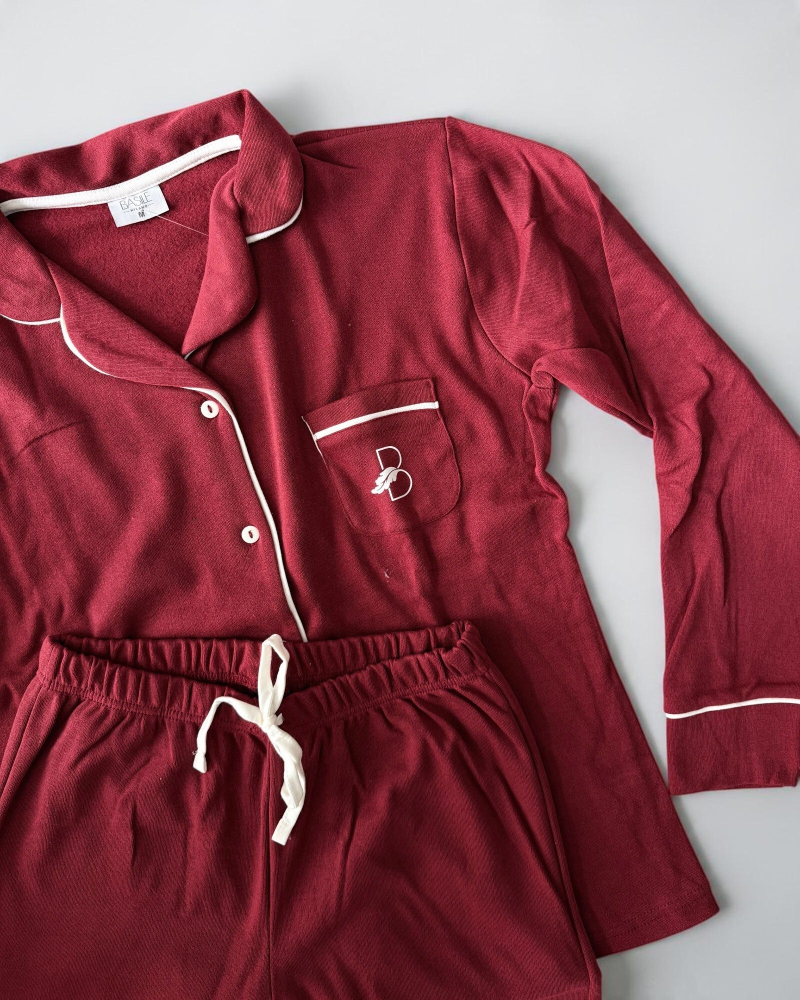 Dettaglio del pigiama bordeaux Basile Milano 4130 con logo sul taschino, piping chiaro e laccetto in vita