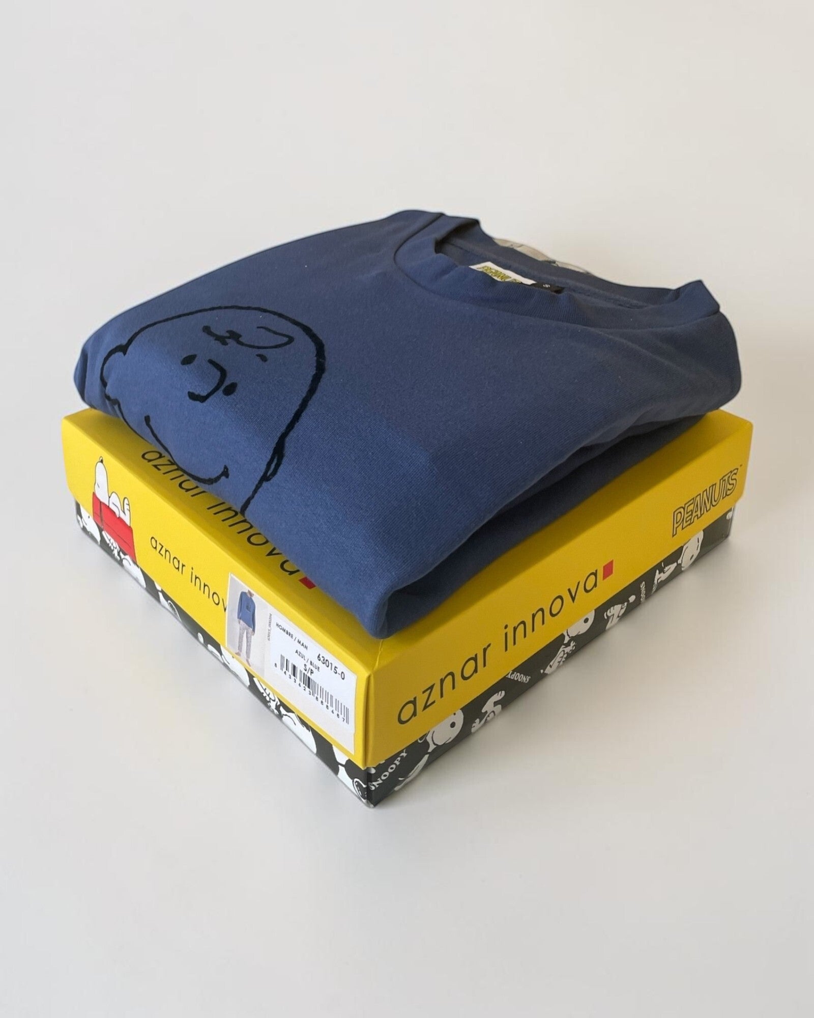 Maglia blu Snoopy e Charlie Brown piegata sopra una scatola regalo gialla Peanuts di Aznar Innova