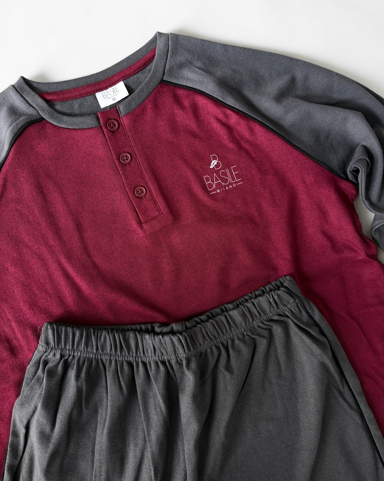 Dettaglio della maglia bordeaux con bottoni e logo Basile Milano, abbinata ai pantaloni grigio scuro