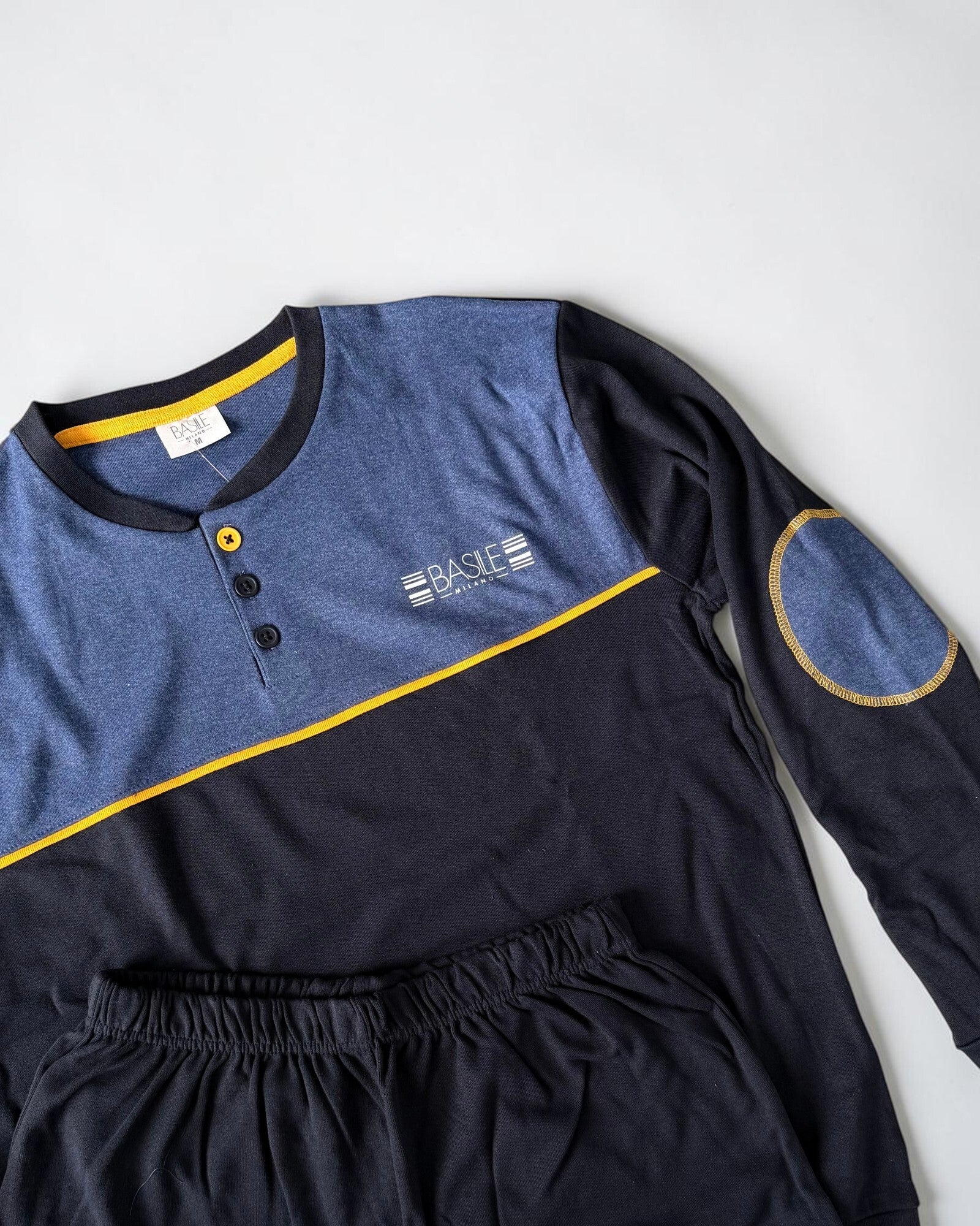 Dettaglio della maglia blu Basile Milano con logo sul petto, toppa sul gomito e bordino giallo