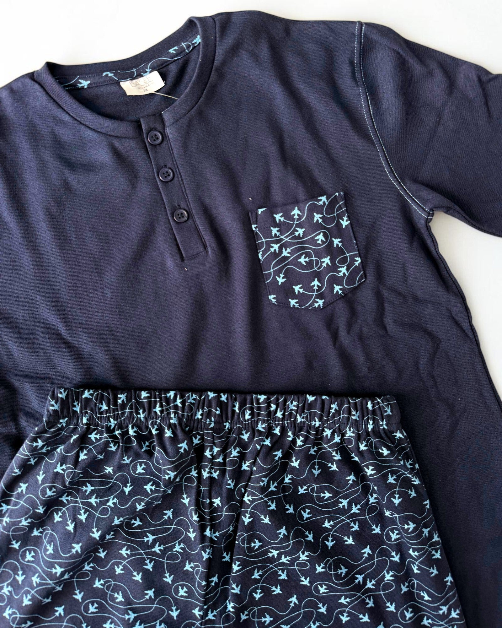 Dettaglio del taschino e dei pantaloni blu con piccoli aeroplani azzurri e linee curve delle rotte di volo