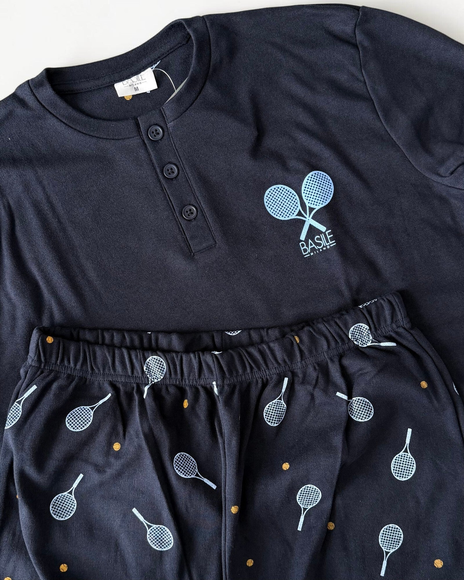 Dettaglio del pigiama blu con racchette incrociate sulla maglia e pantaloni stampati con racchette e palline gialle