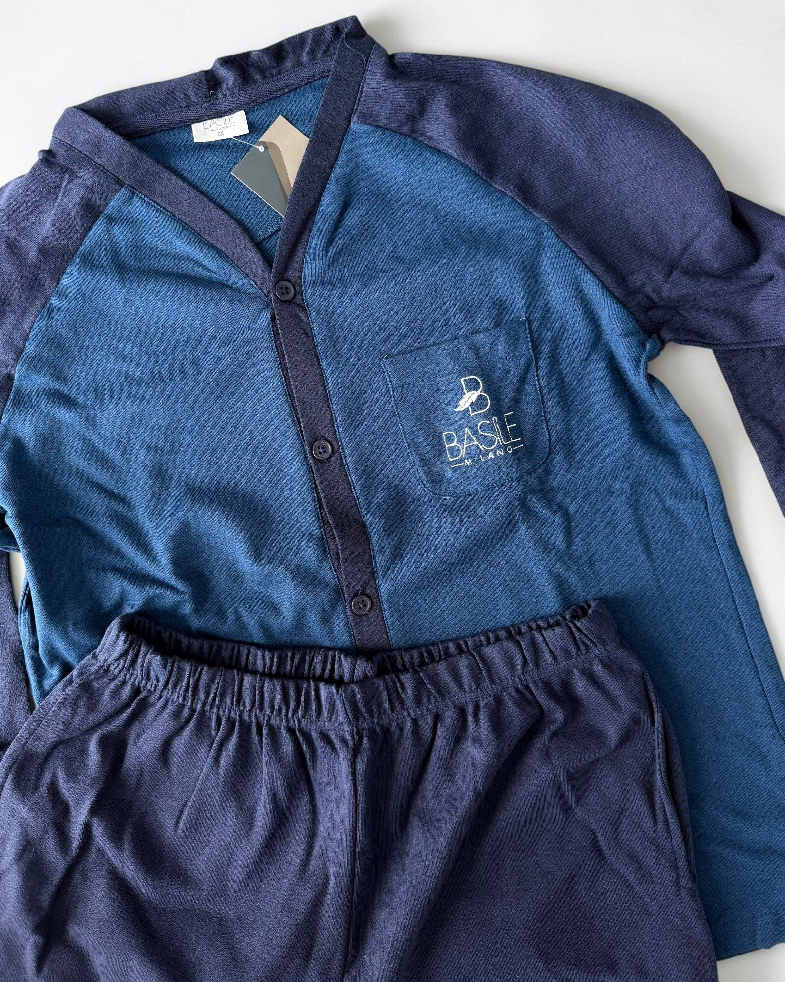 Dettaglio del pigiama ottanio con maniche blu, logo ricamato sul taschino e pantaloni con elastico in vita