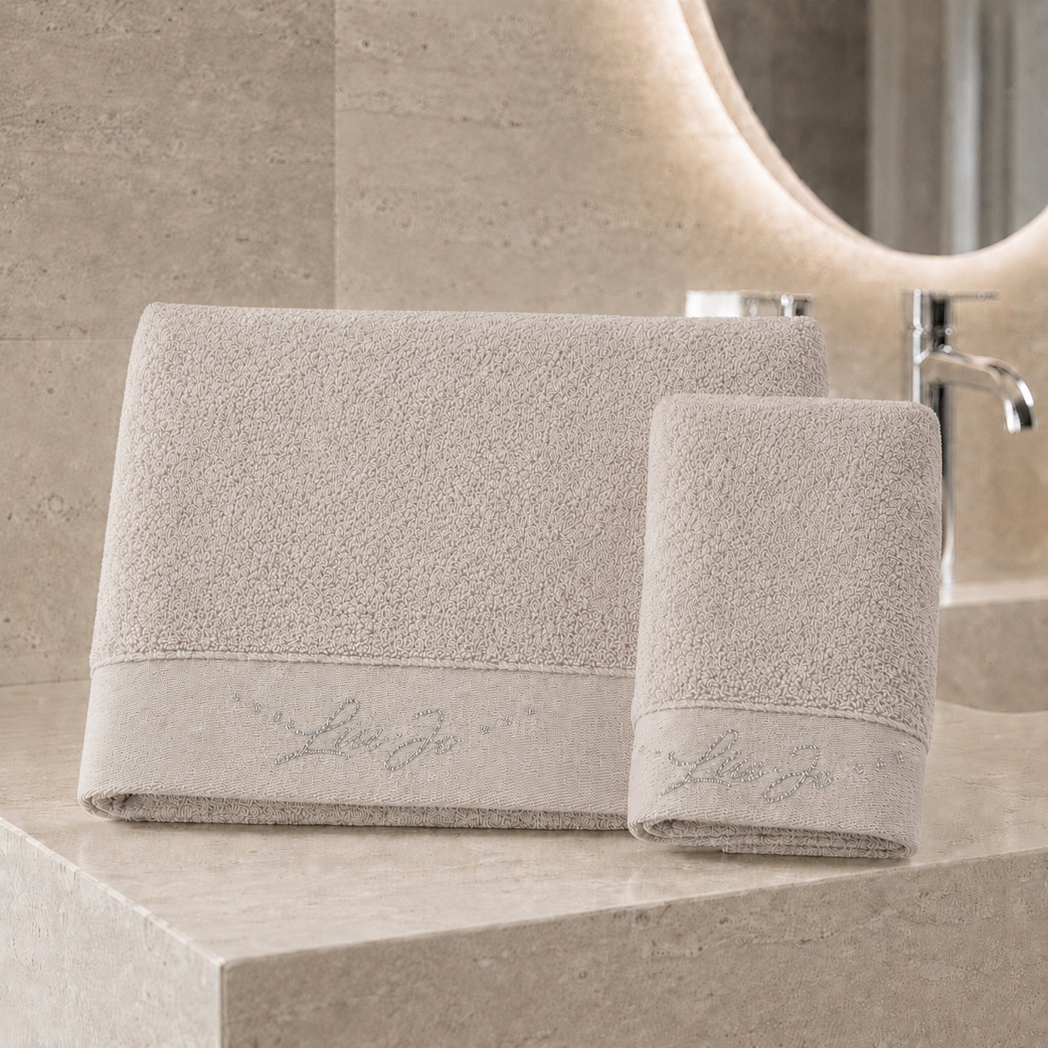 Set asciugamani 1+1 Liu Jo Happy colore tortora con telo viso e ospite ambientati in un bagno elegante