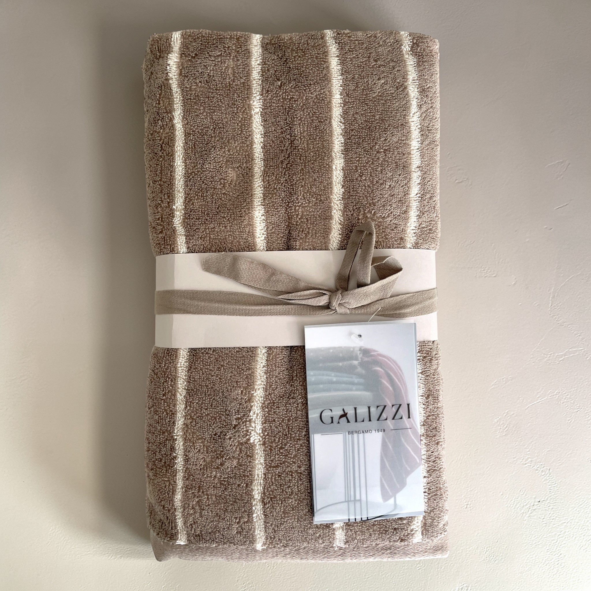 Confezione del set asciugamani Galizzi Saint Louis Noisette, con fascetta, fiocco in tessuto e cartellino Galizzi.