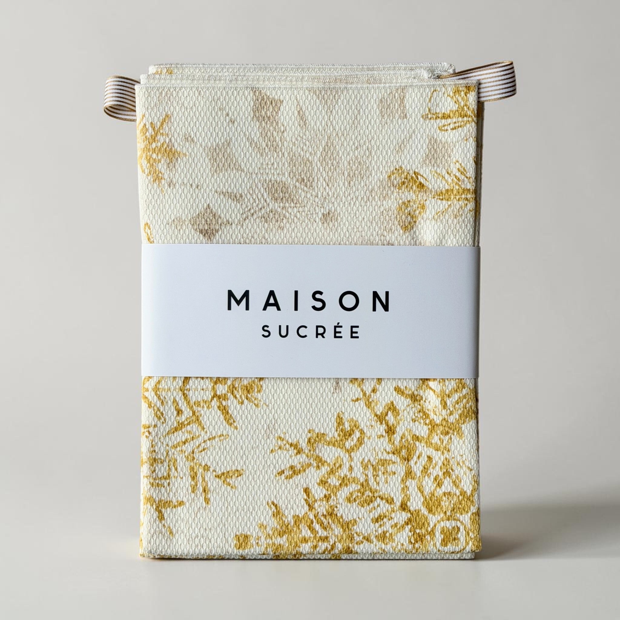Set di due strofinacci Profumi piegati con fascetta Maison Sucrée, fantasia fiocchi di neve e ganci in tessuto a righe.