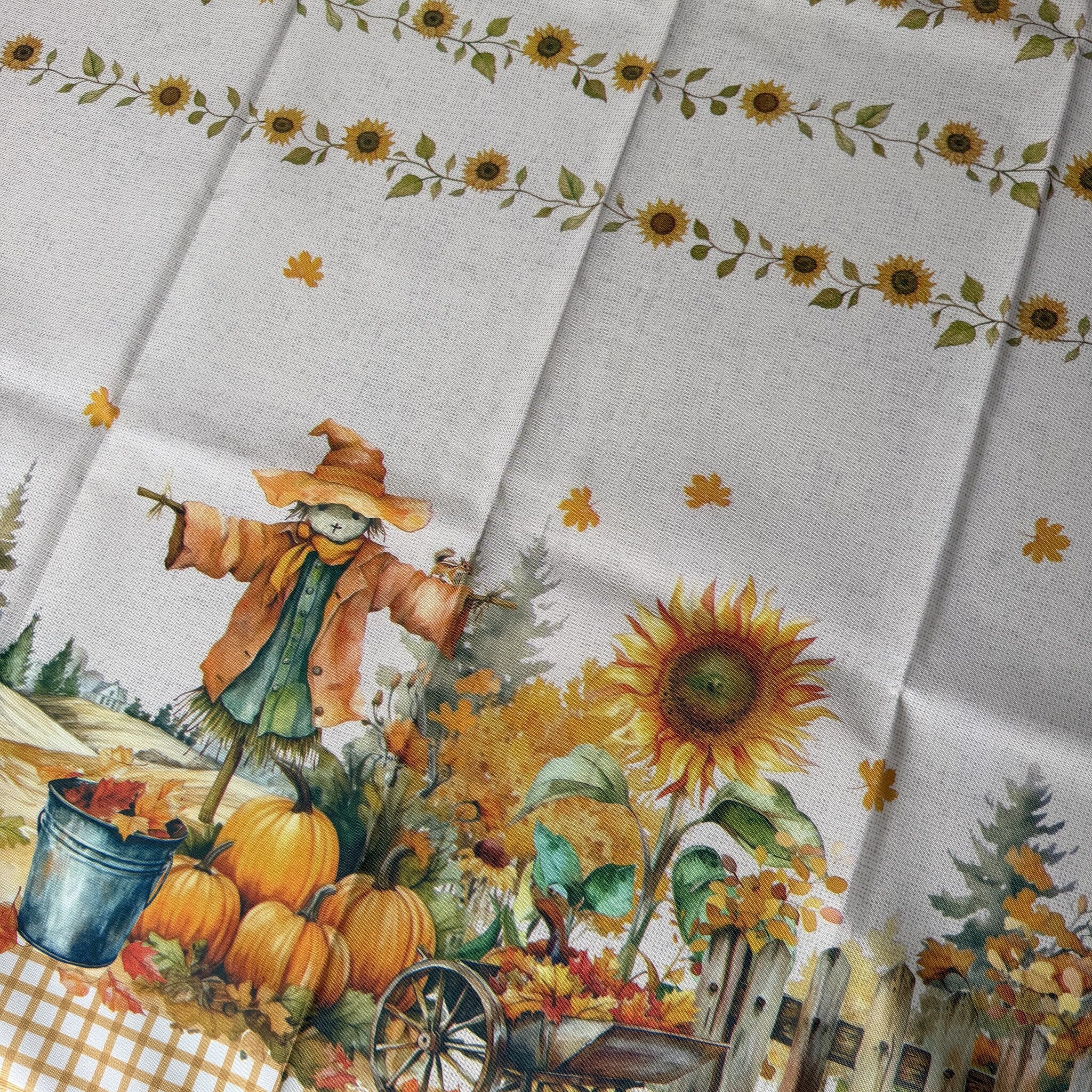Dettaglio del tessuto della tovaglia Amica con spaventapasseri, girasoli, zucche e staccionata.
