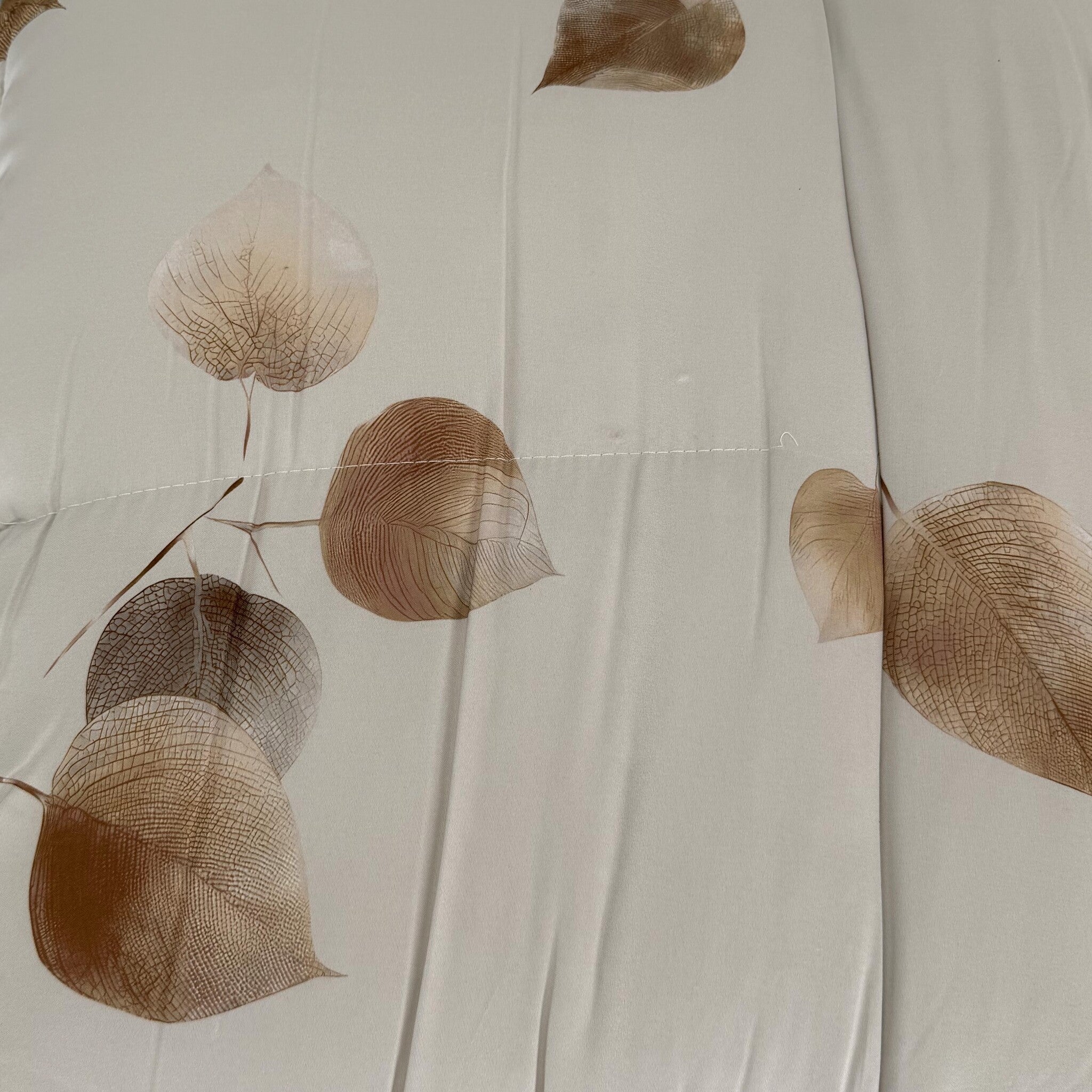 Primo piano del tessuto Cogal 2622 Cognac con foglie beige e marroni su fondo avorio e cucitura della trapuntatura.