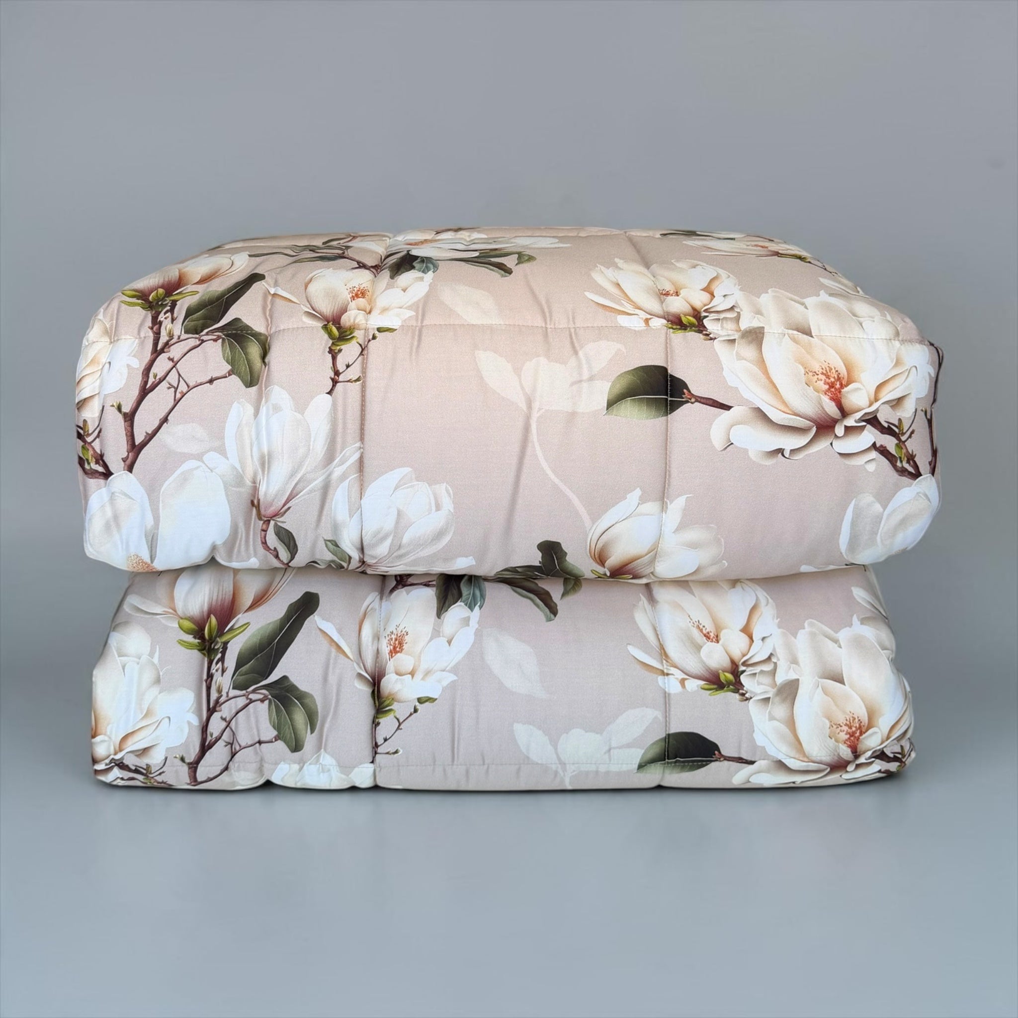 Trapunta Galizzi Lavinia Beige piegata, con stampa di magnolie avorio su fondo neutro e cuciture a riquadri.